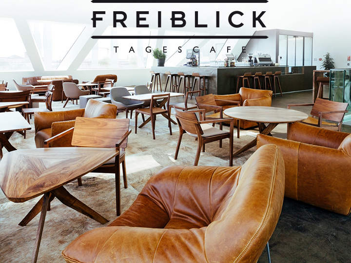 Modernes Café-Interieur mit hellbraunen Lederstühlen, Holztischen und einer minimalistischen Bartheke. Große Fenster sorgen für Tageslicht. Schwarzer Text auf dem Bild lautet „Freiblick Tagescafé“.