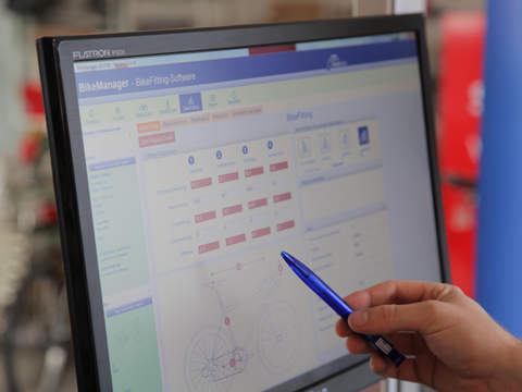 Nahaufnahme einer Person, die einen blauen Stift hält und auf einen Computerbildschirm zeigt, auf dem eine Softwareoberfläche mit Diagrammen und Text angezeigt wird. Der Hintergrund ist leicht verschwommen und zeigt Teile der Ausrüstung.