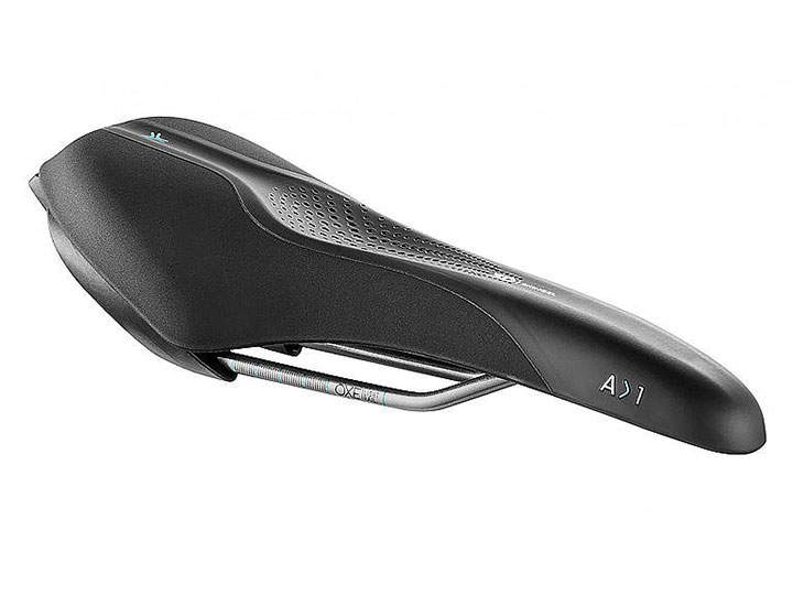 Ein schwarzer Fahrradsattel mit schlankem, aerodynamischem Design. Er verfügt über eine strukturierte Oberfläche mit kleinen Perforationen zur Belüftung und Konturierung. Der Sattel hat ein minimalistisches, modernes Aussehen mit sichtbaren Schienen zur Befestigung.