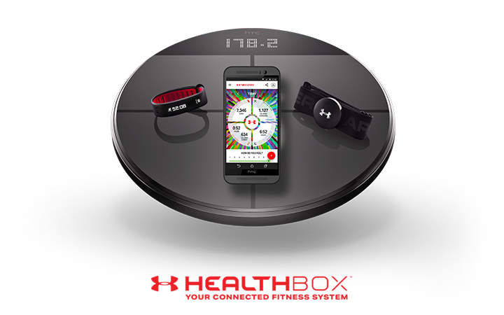 Eine runde Plattform mit drei Fitnessgeräten: eine schwarze Digitalwaage mit der Anzeige „178,2“, ein Smartphone mit einer farbenfrohen Gesundheits-App und ein Brustgurt mit Pulsmessgerät. Der Text darunter lautet „Under Armour Healthbox: Ihr vernetztes Fitnesssystem.“.