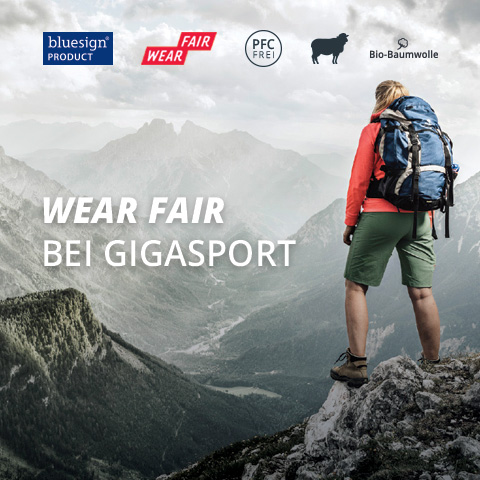 Person in Wanderausrüstung mit Rucksack steht auf einem Felsen mit Blick auf eine weite Berglandschaft. Text lautet „WEAR FAIR BEI GIGASPORT“ mit Ökolabels wie Bluesign, PFC-frei und Bio-Baumwolle.