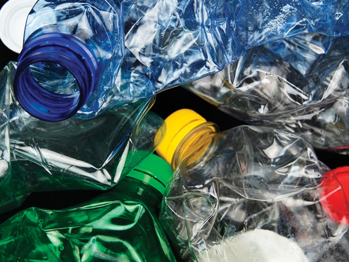 Eine Nahaufnahme zerdrückter Plastikflaschen in verschiedenen Farben, darunter Blau, Gelb, Grün und Rot, die sich auf einem dunklen Hintergrund überlappen. Das Bild hebt die Textur und Transparenz der Plastikmaterialien hervor.