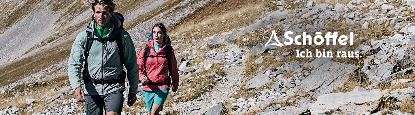 Zwei Wanderer in Outdoor-Ausrüstung gehen einen felsigen Bergpfad entlang. Der Mann trägt eine grüne Jacke und Shorts, die Frau eine rote Jacke und blaugrüne Shorts. Auf der rechten Seite sind das Schöffel-Logo und der Text „Ich bin raus.“ zu sehen.