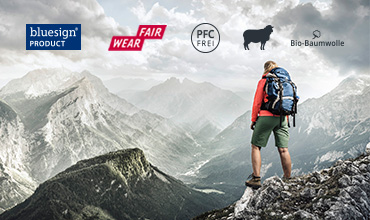 Eine Person in Wanderkleidung steht auf einem Aussichtspunkt in einem felsigen Berg und blickt auf eine weite Landschaft mit schroffen Gipfeln unter einem bewölkten Himmel. Darüber sind mehrere Logos zu sehen, darunter „bluesign“, „Fair Wear“, „PFC Free“ und „Bio-Baumwolle“.