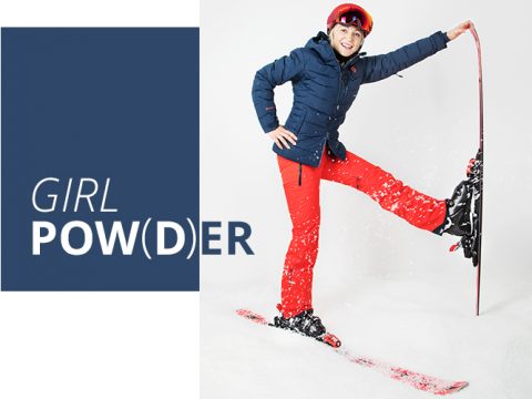Eine Person in Winterkleidung mit blauer Jacke und roter Hose posiert mit einem erhobenen Bein und einem Ski. Sie lächelt und trägt einen roten Helm und eine Schutzbrille. Der Text daneben lautet „GIRL POW(D)ER“.