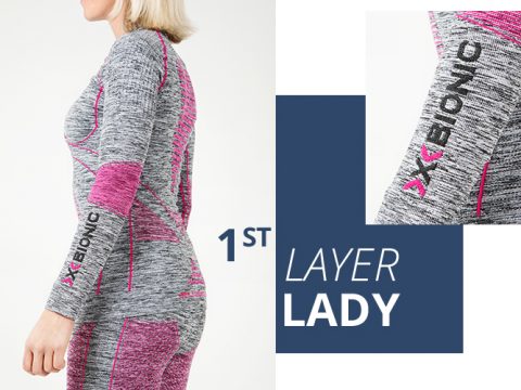 Eine Frau in einem grau-rosa Hightech-Sportoutfit von X-BIONIC steht seitlich. Das Outfit ist mit einem Branding auf dem Arm versehen. Eine Nahaufnahme hebt das Design und das Logo des Ärmels hervor. Der Text lautet „1st Layer Lady“.