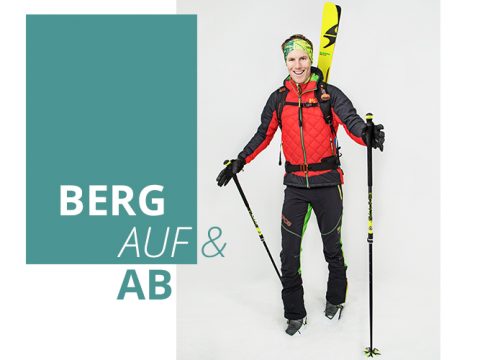 Eine Person in Wintersportkleidung steht mit Skistöcken in der Hand und an den Füßen befestigten Skiern vor einem grauen Hintergrund. Sie lächelt, trägt ein Stirnband und eine rote Jacke. Links steht der Schriftzug „Berg Auf & Ab“.