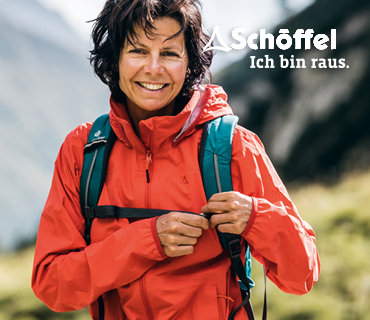 Eine Frau in einer orangefarbenen Jacke mit Rucksack lächelt im Freien. Sie steht vor einem unscharfen natürlichen Hintergrund. In der oberen rechten Ecke erscheint der Text „Schöffel, ich bin raus.“.