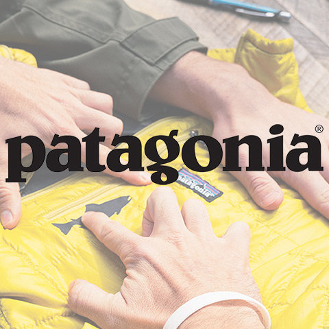 Hände, die an einer gelben Patagonia-Jacke arbeiten. Das Patagonia-Logo ist deutlich über dem Bild zu sehen. Im Hintergrund sind schwach ein Stift und Papier zu erkennen.