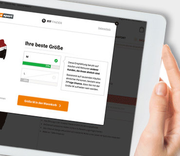 Eine Person hält ein Tablet, auf dem ein Bildschirm mit Größenempfehlungen angezeigt wird. Der Text lautet „Ihre beste Größe“ mit einer Größenauswahltabelle. Ein darunter befindlicher Button lautet „Größe M in den Warenkorb“. Das Tablet wird in einer Hand gehalten, die Finger auf der rechten Seite sind sichtbar.
