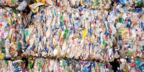 Ballen aus komprimierten Plastikflaschen und -verpackungen, gestapelt. Die Plastikflaschen sind dicht gepackt, in verschiedenen Farben und mit verschiedenen Etiketten erhältlich und bereit zum Recycling. Das Bild zeigt Probleme im Zusammenhang mit Plastikmüll und Recyclingbemühungen.
