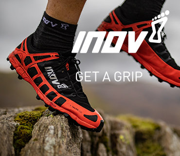 Nahaufnahme einer Person, die schwarze und rote Trailrunning-Schuhe trägt und auf felsigem Gelände läuft. Auf den Schuhen ist das Markenlogo „INOV“ zu sehen. Über dem zerklüfteten Landschaftshintergrund ist der Text „GET A GRIP“ zu sehen.