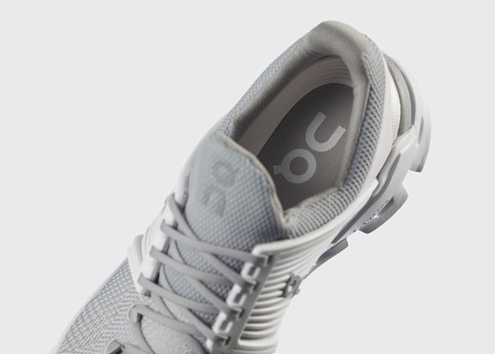 Eine Draufsicht auf einen grauen Sportschuh mit komplexem Profildesign, einem Obermaterial aus strukturiertem Mesh und Schnürsenkeln. Die Innensohle zeigt teilweise ein „ON“-Logo. Der Schuh steht auf einem schlichten weißen Hintergrund.