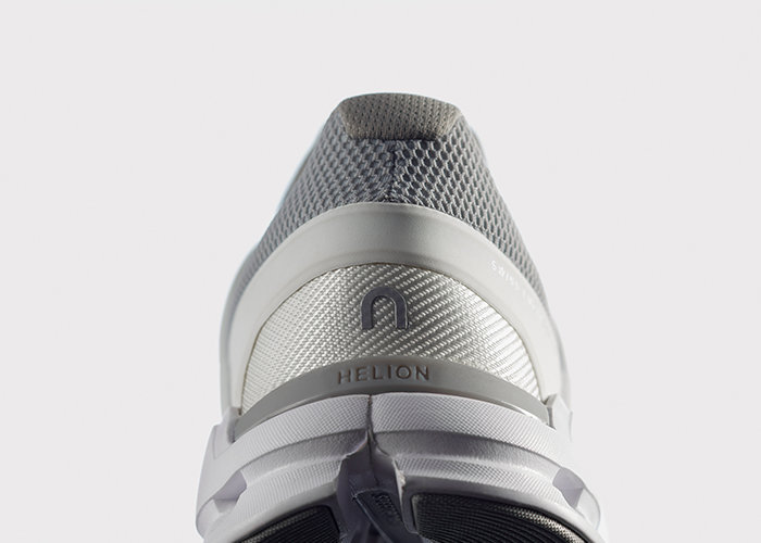 Nahaufnahme der Ferse eines Laufschuhs, die ein grau-weißes Farbschema zeigt. Der Schuh verfügt über ein strukturiertes Mesh-Design und das Wort „HELION“ ist auf der Ferse eingeprägt, was ihm eine elegante und moderne Ästhetik verleiht.