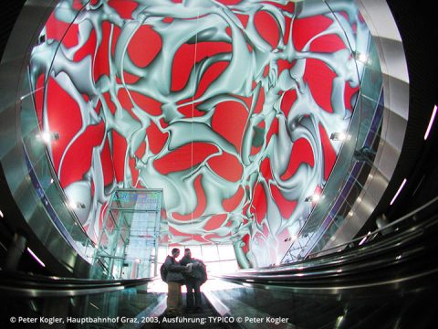 Eine lebendige, abstrakte Kunstinstallation von Peter Kogler schmückt die Decke des Grazer Hauptbahnhofs. Sie zeigt wirbelnde rote, graue und weiße Muster, die im geräumigen, modernen Inneren des Bahnhofs einen dynamischen, eindringlichen Effekt erzeugen.