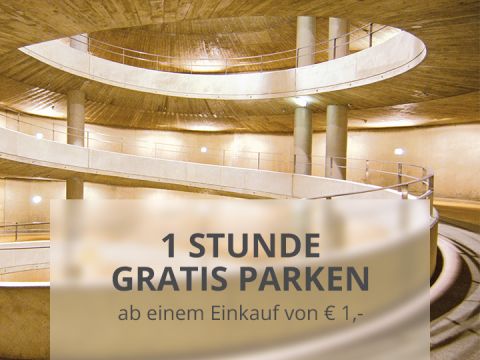 Spiralförmige Rampe in einem Parkhaus mit einem Werbeschild mit der Aufschrift „1 Stunde gratis parken ab einem Einkauf von €1,-“ auf Deutsch, das eine Stunde kostenloses Parken ab einem Einkauf von 1 € anbietet.