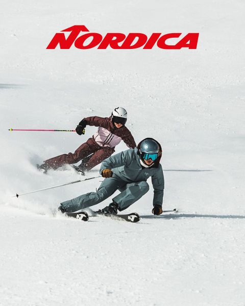 Zwei Skifahrer in Schutzausrüstung – einer in blauer, der andere in dunkler Kleidung – fahren im Schnee bergab. Das „Nordica“-Logo ist oben zu sehen. Beide sind schräg gestellt und demonstrieren Schnelligkeit und Beweglichkeit an einem sonnigen Tag.