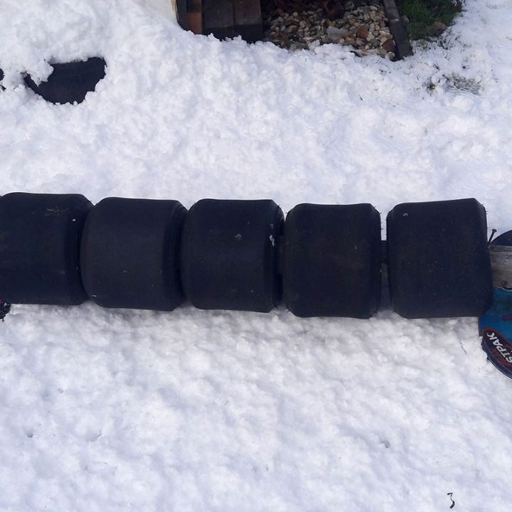 Ein selbstgebauter Schlitten aus fünf schwarzen Gummirädern, die an einem Holzbrett befestigt sind und an jedem Ende über Bindungen an Skibretter verfügen und auf dem Schnee ruhen.