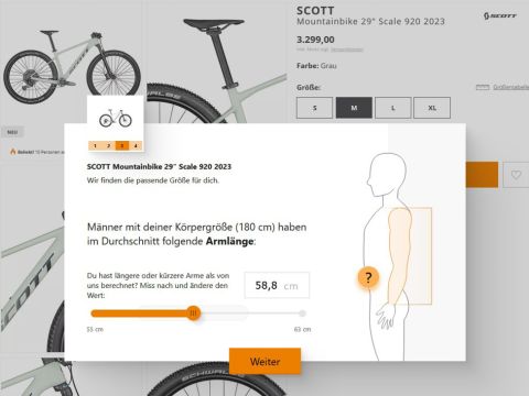 Ein Screenshot einer Webseite, die ein graues Scott-Mountainbike mit seinen Spezifikationen und einem Preis von 3.299,00 zeigt. Ein Overlay-Popup gibt Hinweise zur Armlängenmessung und hebt 58,8 cm für eine etwa 180 cm große Person hervor. Schaltflächen zur Navigation sind sichtbar.