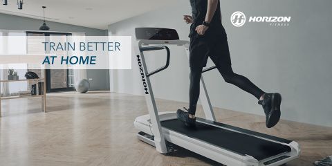Person, die auf einem Laufband von Horizon Fitness in einem modernen, geräumigen Raum mit Holzboden und großen Fenstern läuft. Neben dem Logo von Horizon Fitness steht der Text „Trainiere besser zu Hause“.