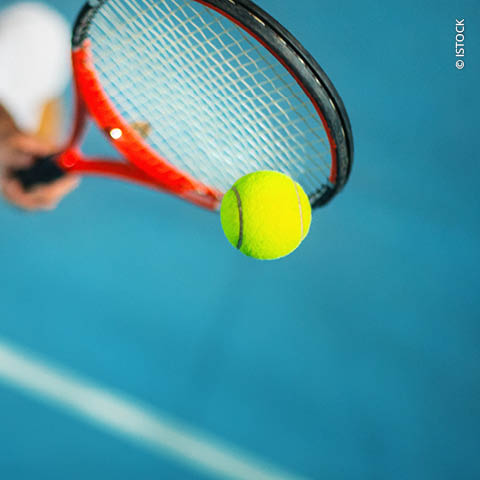 Nahaufnahme eines Tennisschlägers mit rotem Rahmen, der vor einem unscharfen blauen Hintergrund einen leuchtend gelben Tennisball trifft, was an eine Action-Aufnahme eines Tennisspiels erinnert.