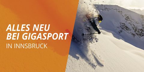 Ein Skifahrer fährt einen verschneiten Berg hinunter. Der Schnee spritzt auf. Auf der linken Seite des Bildes ist ein orangefarbenes Banner mit dem Text „Alles Neu bei Gigasport in Innsbruck“ zu sehen. Im Hintergrund sind Berge zu sehen.