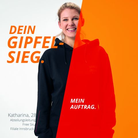 Eine junge Frau in einem schwarzen Kapuzenpullover lächelt in die Kamera. Das Bild ist geteilt und rechts mit einer orangefarbenen Überlagerung versehen. Der Text lautet „DEIN GIPFELSIEG“. und „MEIN AUFTRAG.“ Darunter steht: „Katharina, 28, Abteilungsleitung Free Ski, Filiale Innsbruck.“.