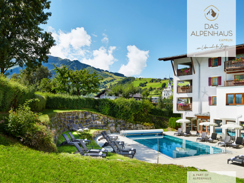 Außenpoolbereich eines Hotels, umgeben von Liegestühlen und üppigem Grün. Auf der rechten Seite befindet sich ein modernes Gebäude mit Balkonen und im Hintergrund sanfte Hügel und ein klarer blauer Himmel. Das Logo „Das Alpenhaus Kaprun“ befindet sich in der oberen rechten Ecke.