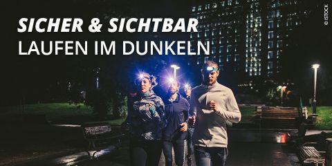 Vier Personen joggen nachts mit Stirnlampen auf einem schwach beleuchteten Weg. Im Hintergrund sind beleuchtete Gebäude zu sehen. Der Text lautet „Sicher & Sichtbar Laufen im Dunkeln“ und weist auf die Sichtbarkeit beim Laufen im Dunkeln hin.