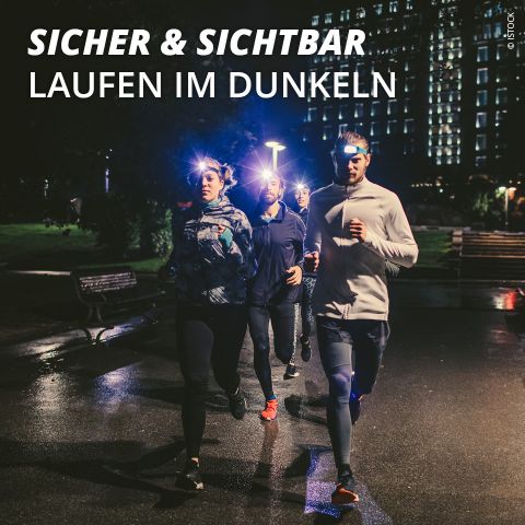 Fünf Leute joggen nachts in einem Park und tragen Stirnlampen, um besser gesehen zu werden. Der Text oben lautet „SICHER & SICHTBAR LAUFEN IM DUNKELN“. Die Umgebung ist schwach beleuchtet, im Hintergrund sind Gebäude und Bäume zu sehen.