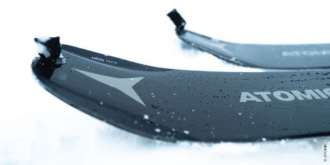 Nahaufnahme von zwei schwarzen Skiern mit Wassertropfen darauf, die auf Schnee liegen. Auf den Skiern steht das Wort „ATOMIC“ und ein Sternlogo. Die Spitzen sind leicht erhöht und der Fokus liegt auf der Textur und den Details.