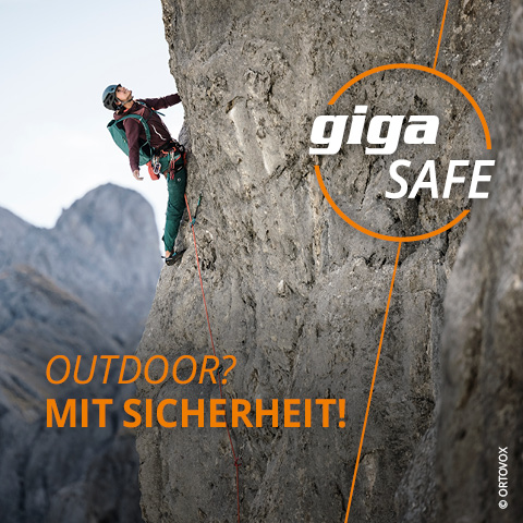 Ein Kletterer erklimmt eine steile Felswand in den Bergen, gesichert mit einem roten Seil. Der Text „giga SAFE“ und „OUTDOOR? MIT SICHERHEIT!“ überlagert das Bild. Der Hintergrund zeigt schroffes Berggelände in wolkiger Atmosphäre.