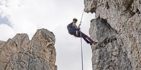 Eine Person in Kletterausrüstung seilt sich eine steile Felswand hinab, die von hoch aufragenden Felsformationen umgeben ist. Der Himmel ist bedeckt und schafft eine dramatische Kulisse für die Outdoor-Abenteuerszene.
