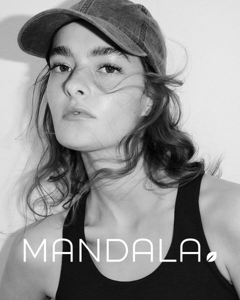 Frau mit Mütze und schwarzem Tanktop blickt direkt in die Kamera. Ihr Haar ist wellig und offen. Das Bild ist schwarz-weiß und trägt unten in großen Buchstaben das Wort „MANDALA“.