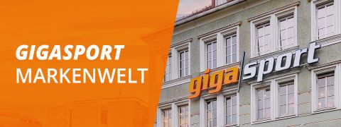 Ein Gebäude, an dessen Außenseite teilweise in großen Lettern „gigasport“ steht. Links ist auf einer orangefarbenen Tafel in fetten weißen Lettern der Schriftzug „GIGASPORT MARKENWELT“ zu sehen.