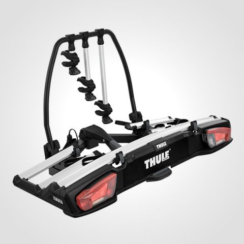 Ein schwarz-silberner Thule-Fahrradträger mit Rücklichtern, der zur Befestigung an der Anhängerkupplung eines Fahrzeugs vorgesehen ist. Er verfügt über verstellbare Arme zur Sicherung von Fahrrädern. Der Markenname „Thule“ ist sichtbar. Der Hintergrund ist schlicht hellgrau.