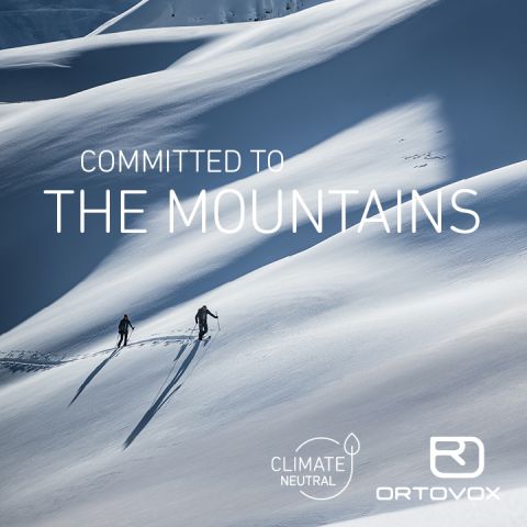 Zwei Menschen wandern unter strahlend blauem Himmel durch eine verschneite Berglandschaft. Auf den Texten steht „Engagement für die Berge“, „Klimaneutral“ und „Ortovox“ mit Logos.