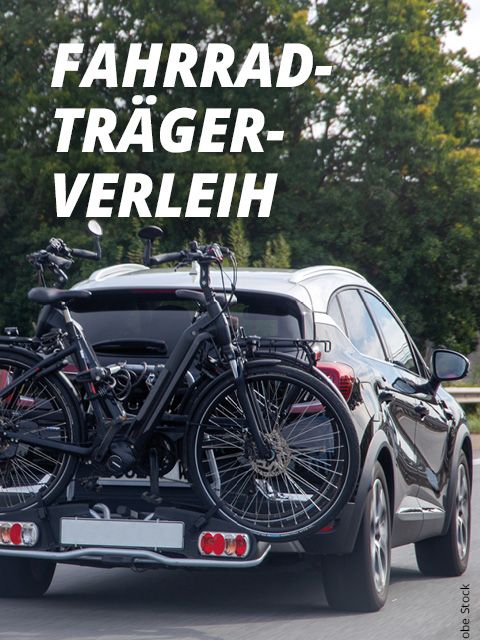 Ein Auto fährt mit zwei Fahrrädern auf einem Gepäckträger auf einer Straße. Im Hintergrund sind grüne Bäume zu sehen. In großer weißer Schrift steht „FAHRRADTRÄGERVERLEIH“.