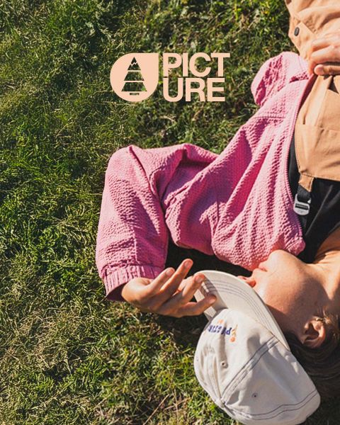 Person liegt im Gras und trägt eine rosa strukturierte Jacke und eine weiße Mütze. Die Hand liegt nah am Gesicht und verdeckt es teilweise. In der oberen linken Ecke ist die Marke „Picture“ zu sehen.