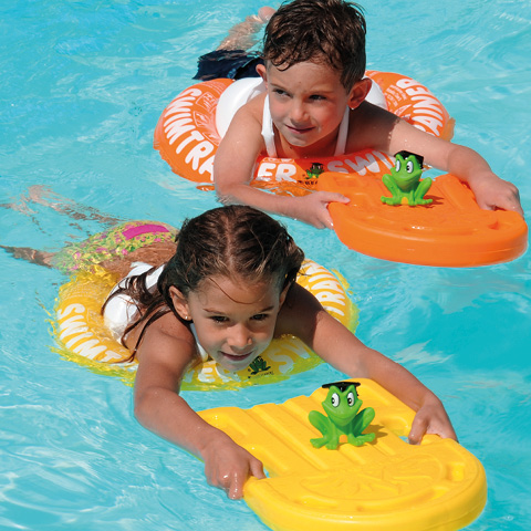 Zwei Kinder schwimmen in einem Pool auf orangefarbenen und gelben Schwimmbrettern mit Froschmotiven. Sie tragen Schwimmringe um die Hüften und genießen das Wasser. Beide lächeln und scheinen Spaß zu haben.