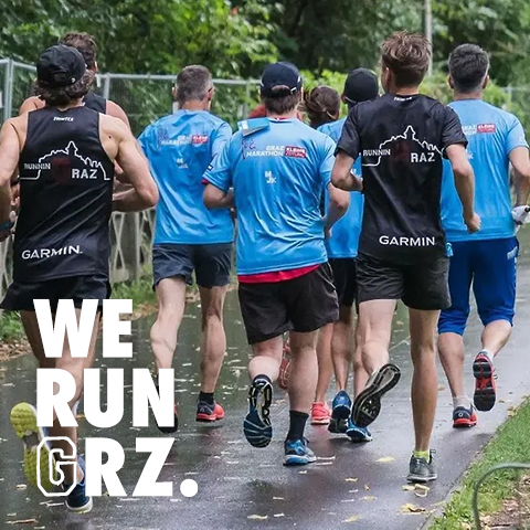 Eine Gruppe Läufer in schwarz-blauen „GARMIN“-Shirts nimmt an einem Lauf im Freien auf einem gepflasterten, von Bäumen umgebenen Weg teil. In der unteren linken Ecke ist der Text „WE RUN GRZ.“ zu sehen.