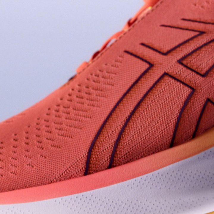 Nahaufnahme eines Sneakers mit strukturiertem, korallenrosa Obermaterial und aufgenähten abstrakten Mustern. Der Schuh hat dezente Perforationen für mehr Atmungsaktivität und sitzt auf einer weiß-orangefarbenen Zwischensohle.