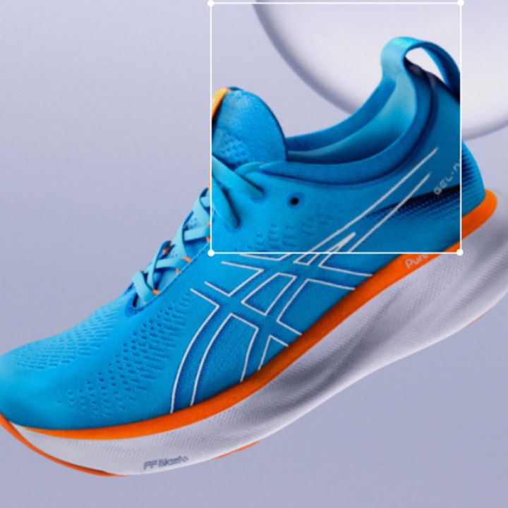 Nahaufnahme eines türkisfarbenen Sportschuhs mit zwei Logos. Der Schuh hat blaue Schnürsenkel, eine strukturierte Oberfläche und gelbe Akzente im Öffnungsbereich. Eine Hand hält den Schuh, der so angewinkelt ist, dass die Seiten- und Draufsicht zu sehen ist.