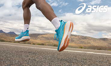 Nahaufnahme einer Person, die in leuchtend blauen und orangefarbenen ASICS-Laufschuhen auf einer Straße läuft. Der Hintergrund zeigt eine malerische Landschaft mit Bergen und einem teilweise bewölkten Himmel. Das ASICS-Logo ist in der oberen rechten Ecke sichtbar.