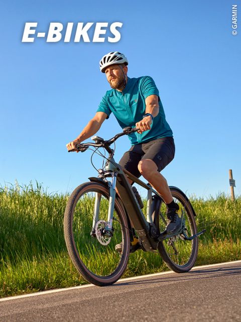 Ein Mann in blauem Hemd und Helm fährt an einem sonnigen Tag mit einem E-Bike. Im Hintergrund ist grünes Gras und ein klarer blauer Himmel zu sehen. Oben ist das Wort „E-BIKES“ zu sehen.