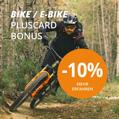 Ein Radfahrer mit Helm und Sonnenbrille fährt mit einem Mountainbike auf einem Waldweg. Der Text lautet: „Bike/E-Bike Pluscard Bonus“ mit einem großen orangefarbenen Kreis mit der Aufschrift „-10 % Mehr Erfahren“.