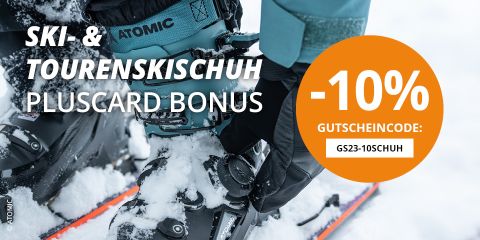 Nahaufnahme einer Person in Winterkleidung, die auf einem schneebedeckten Hang schwarze Skibindungen einstellt. Der Text auf dem Bild bietet mit einem Promo-Code mit Atomic-Branding 10 % Rabatt auf Skischuhe.