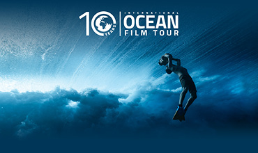 Ein Taucher schwimmt unter Wasser im tiefblauen Ozean. Der Text lautet: „10 Jahre Internationale Ozean-Filmtour“. Sonnenlicht fällt durch das Wasser und erzeugt ein Strahlenmuster.