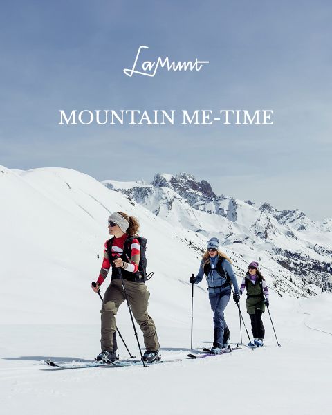 Drei Personen in Winterkleidung fahren unter klarem Himmel Ski durch eine verschneite Berglandschaft. Der Text lautet: „LaMunt MOUNTAIN ME-TIME“. Im Hintergrund sind schneebedeckte Gipfel zu sehen.