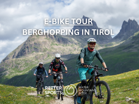 Drei Personen fahren mit E-Bikes auf einem Bergpfad in Tirol, umgeben von üppig grünen Hügeln und hohen Gipfeln unter einem wolkigen Himmel. Der Text auf dem Bild lautet: „E-Bike-Tour Berghüpfen in Tirol“ mit Logos von Retter Sports und Water Mountain Body.